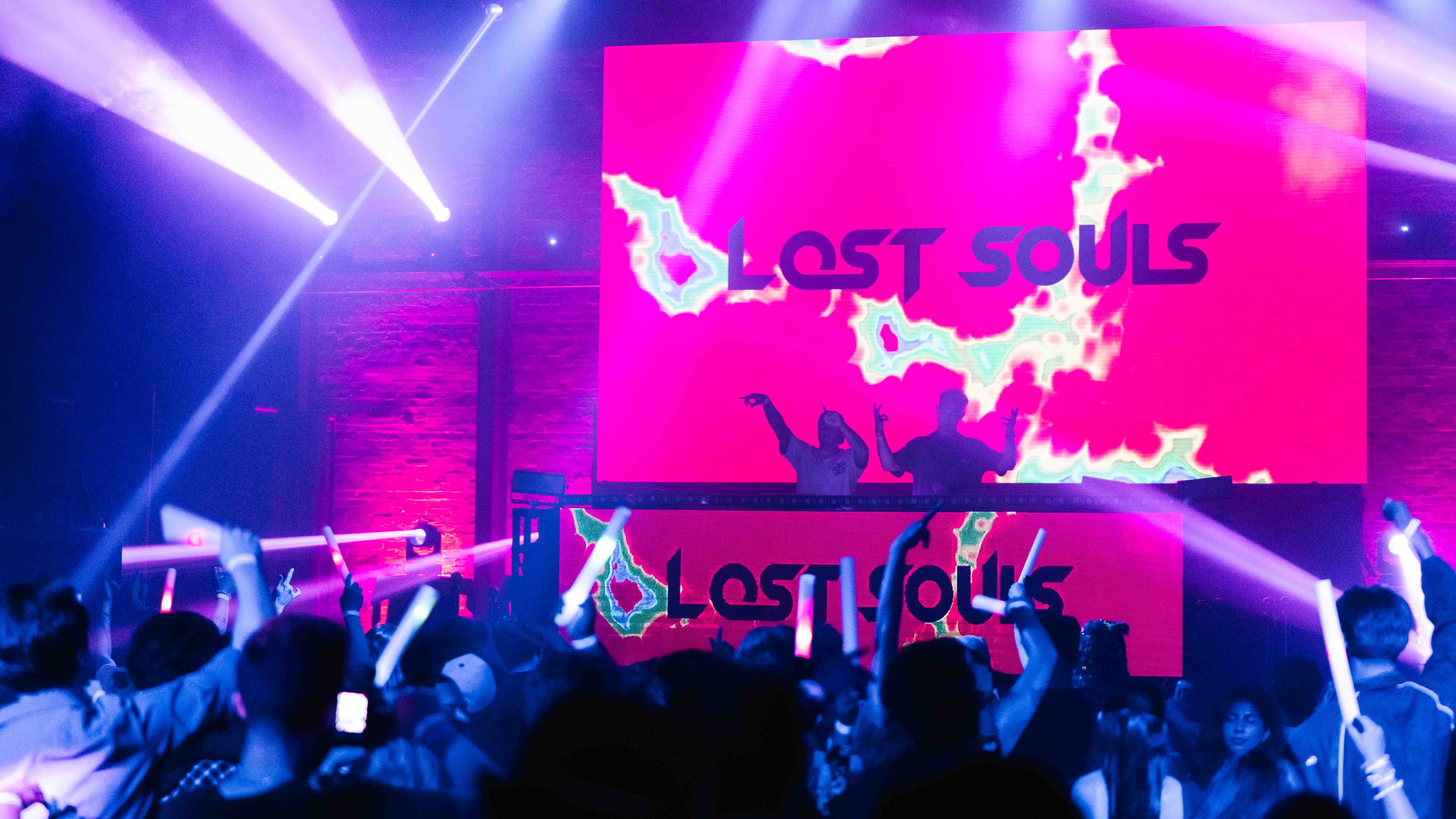 Concert crowd with arms raised in unison silhouetted against electric blue stage wash